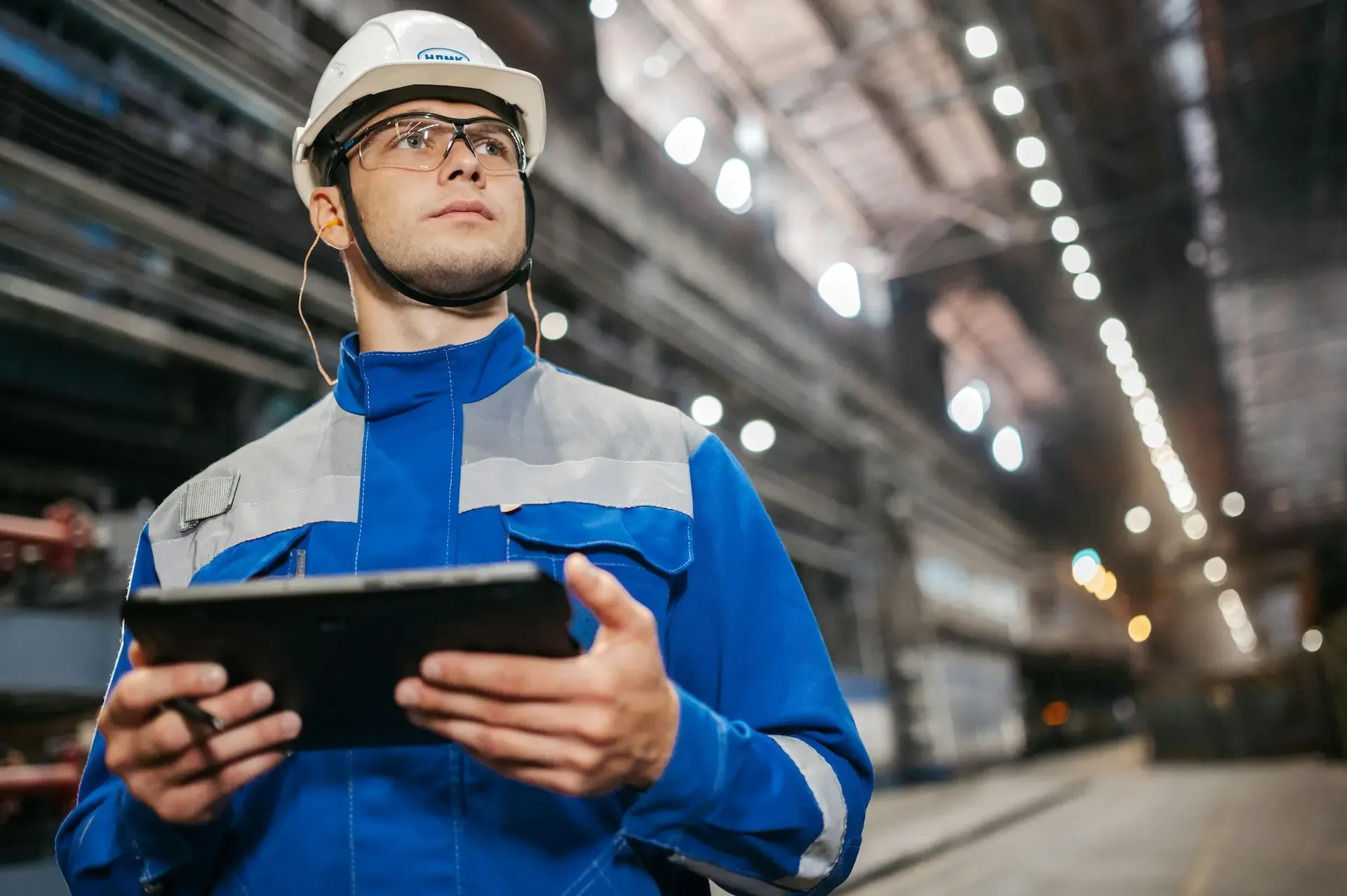 Ingeniero con equipo de seguridad revisando los datos de control en una tablet dentro de una planta industrial